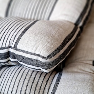 May include: Close-up of two textured pillows. The pillows are white with vertical black stripes and black borders. The fabric appears to be linen or a similar natural material. The pillows are stacked on top of each other.