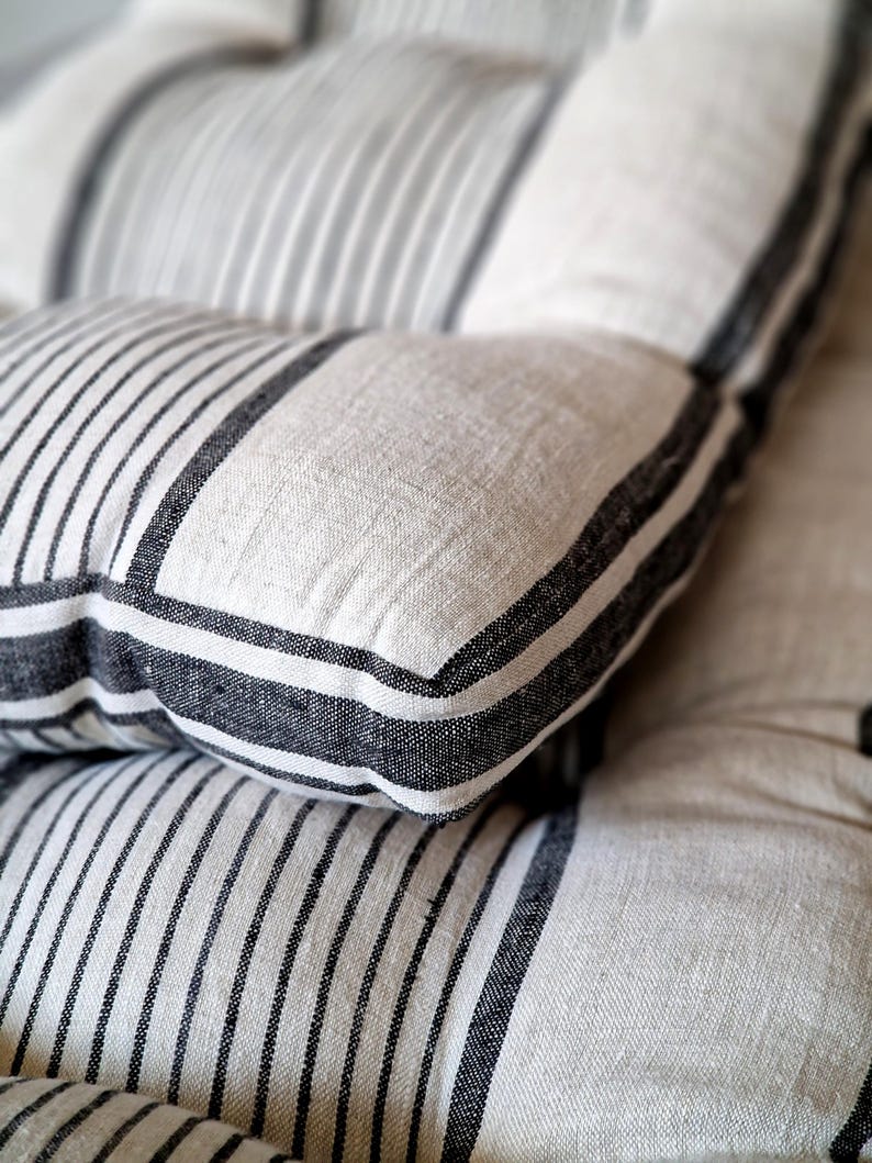 May include: Close-up of two textured pillows. The pillows are white with vertical black stripes and black borders. The fabric appears to be linen or a similar natural material. The pillows are stacked on top of each other.