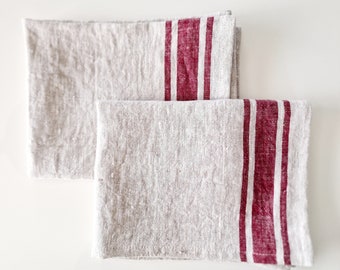 May include: Two linen tea towels with red stripes. The towels are folded and stacked on top of each other.