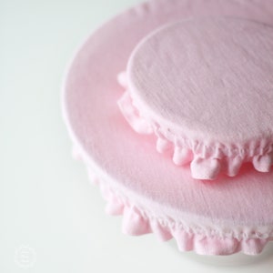Two soft blush pink linen bowl covers in different sizes. Close-up of eco-friendly fabric dish covers with elastic ruffled edges, showing the natural linen texture. Minimalist zero waste kitchen accessories and plastic wrap alternative.