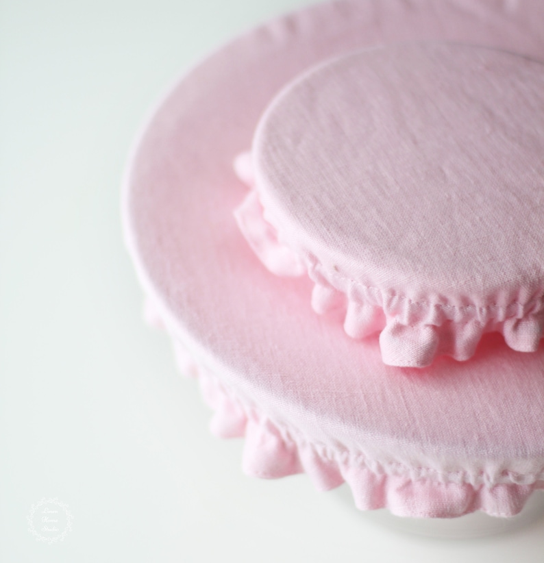 Two soft blush pink linen bowl covers in different sizes. Close-up of eco-friendly fabric dish covers with elastic ruffled edges, showing the natural linen texture. Minimalist zero waste kitchen accessories and plastic wrap alternative.