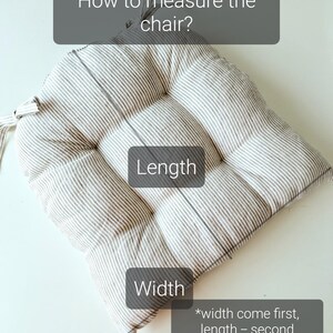 Graphic guide on how to measure a chair for a striped linen seat cushion. The image shows a square, tufted grey and white striped kitchen chair pad on a white table. Three dark grey text boxes explain the dimensions: 'Length' indicates the vertical measurement, 'Width' shows the horizontal front edge, and a note explains that width comes first (e.g., 43cm width by 39cm length).