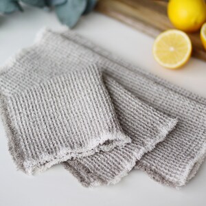 May include: Two gray waffle weave kitchen towels with frayed edges. The towels are folded and stacked on top of each other.