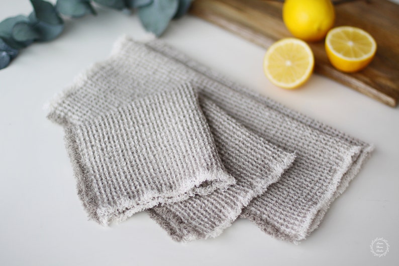May include: Two gray waffle weave kitchen towels with frayed edges. The towels are folded and stacked on top of each other.