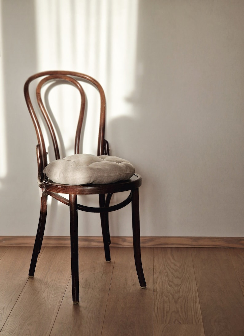 Puede incluir: Una silla de madera con un coj&iacute;n de color marr&oacute;n claro en el asiento. La silla est&aacute; en una habitaci&oacute;n con un suelo de madera clara y una pared blanca.