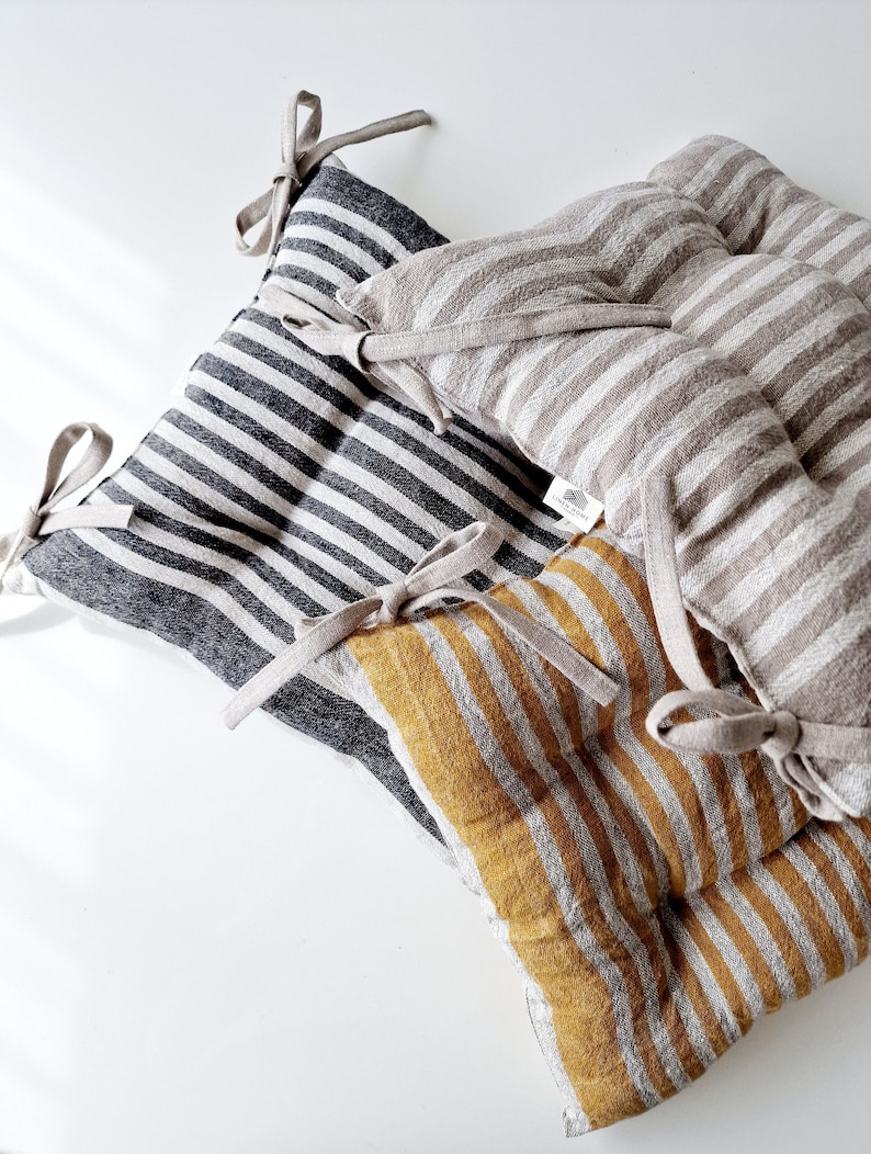 Puede incluir: Tres cojines de silla de lino a rayas con lazos. Los cojines son en blanco y negro, beige y blanco, y amarillo mostaza y blanco.