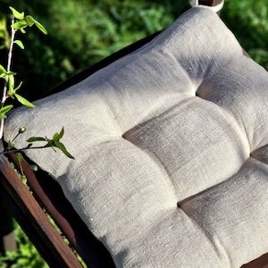 Puede incluir: Un coj&iacute;n de silla de lino beige con un dise&ntilde;o capiton&eacute;. El coj&iacute;n est&aacute; colocado en una silla de madera.