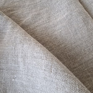Peut inclure: Gros plan sur un tissu tissé gris clair avec une texture subtile. Le tissu est plié en deux, créant une ligne diagonale à travers l'image.