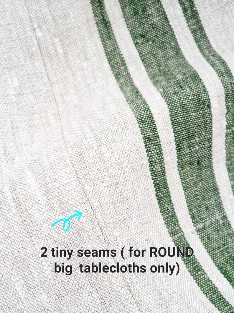 Extreme close-up of a high-quality joined seam on a heavyweight oatmeal linen tablecloth with forest green stripes. A blue arrow points to the discreet 'tiny seam' used for extra-wide round tablecloths. The image highlights the professional craftsmanship and natural, rustic flax texture