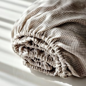 Puede incluir: Una sábana bajera de cuadros marrones y blancos enrollada. La sábana está hecha de un tejido suave y natural.