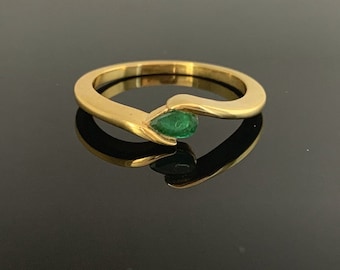 May include: A gold ring with a teardrop-shaped emerald gemstone. The ring has a smooth, polished finish and a modern, minimalist design. The emerald is a vibrant green color and is set in a bezel setting.