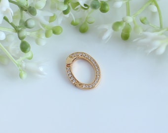 Puede incluir: Un charm ovalado de oro con un borde de cristal transparente. El charm tiene una abertura con bisagra.