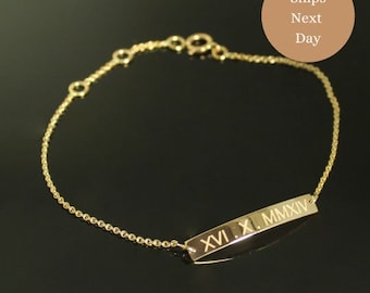 Op de afbeelding: Een goudkleurige armband met een fijne ketting en een rechthoekige hanger. De hanger is gegraveerd met Romeinse cijfers. De afbeelding bevat een cirkelvormige afbeelding met de tekst "Ships Next Day".