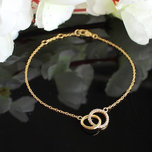 May include: A gold chain bracelet featuring two interlocking circles set with small clear stones.