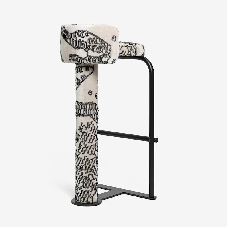 May include: A modern bar stool with a black metal frame and a patterned seat and backrest. The seat and backrest are upholstered in a cream-colored fabric with a black, abstract design. The stool has a footrest and a round base.
