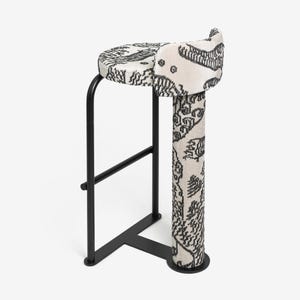 May include: A modern bar stool with a black metal frame and a patterned seat and backrest. The seat and backrest feature a cream-colored fabric with a black, intricate design. The stool's design is minimalist and stylish.