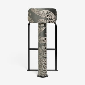 May include: A modern bar stool with a rectangular, upholstered seat and a patterned design in shades of gray and beige. The stool has a black metal frame and a cylindrical central support. The overall design is contemporary and stylish.