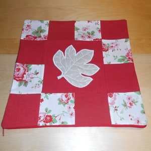 Könnte beinhalten: Rotes und weißes Patchwork-Kissen mit einem weißen gestickten Blattmotiv.