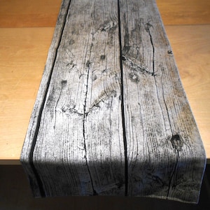 Könnte beinhalten: Ein grauer und schwarzer Tischläufer mit Holzmaserung. Der Läufer hat einen schwarzen Rand und ist aus Stoff.