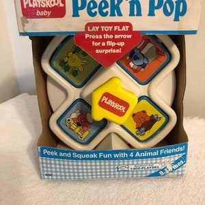 May include: A white plastic toy with four colorful squares that flip up to reveal animal faces. The toy is labeled "Playskool Peek 'n Pop" and is for ages 9-30 months.