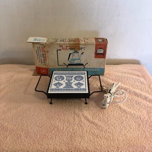 Puede incluir: Calentador de alimentos eléctrico vintage con marco de metal negro y tapa de azulejo decorativo con diseños azules y blancos. La caja dice "hot-server" y "ELECTRIC FOOD WARMER". Incluye un cable de alimentación blanco.