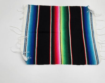 May include: A colorful striped Mexican blanket with black, blue, green, red, yellow, and white stripes. The blanket has frayed edges and is made of woven fabric.