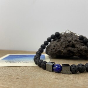 Può includere: Un braccialetto di perline di roccia vulcanica nera con due perline cubiche di ematite nera e una perla di lapislazzuli blu.