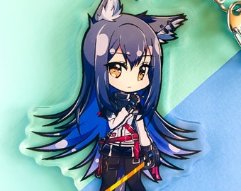 May include: A clear acrylic keychain featuring a cartoon anime character with blue hair, a white shirt, black pants, and a yellow sword. The character has wolf ears and a tail. The keychain is on a blue and green background. The text "©イモキ" is on the bottom of the keychain.