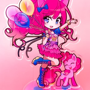 May include: Pinkie Pie from My Little Pony is depicted in a chibi style, wearing a blue and pink outfit with a cupcake design. She is holding balloons and has a pink pony by her side. The image is on a clear acrylic stand with a pink base.