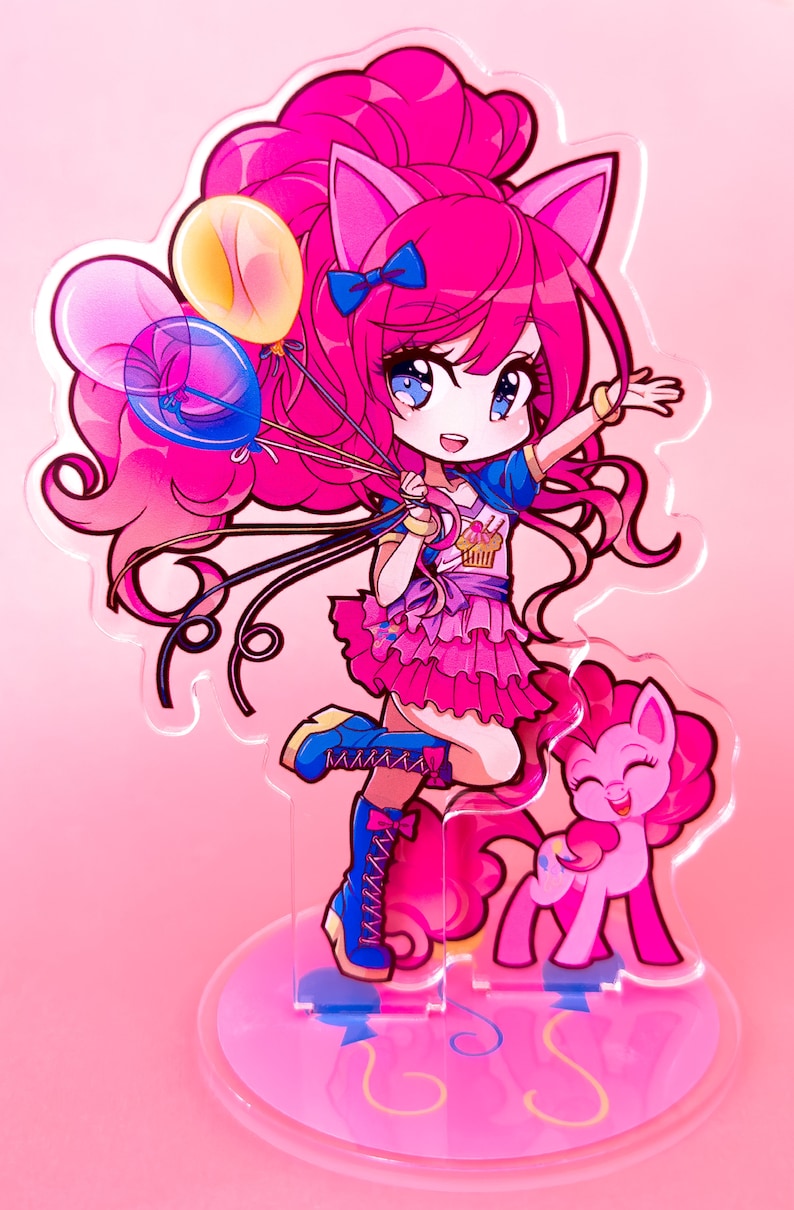 May include: Pinkie Pie from My Little Pony is depicted in a chibi style, wearing a blue and pink outfit with a cupcake design. She is holding balloons and has a pink pony by her side. The image is on a clear acrylic stand with a pink base.