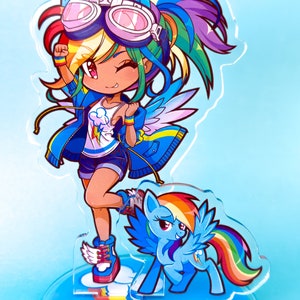 May include: A colorful acrylic stand featuring a cartoon character with rainbow hair, blue wings, and a blue jacket. The character is wearing goggles and has a rainbow tail. The stand also features a smaller cartoon pony with a rainbow tail.