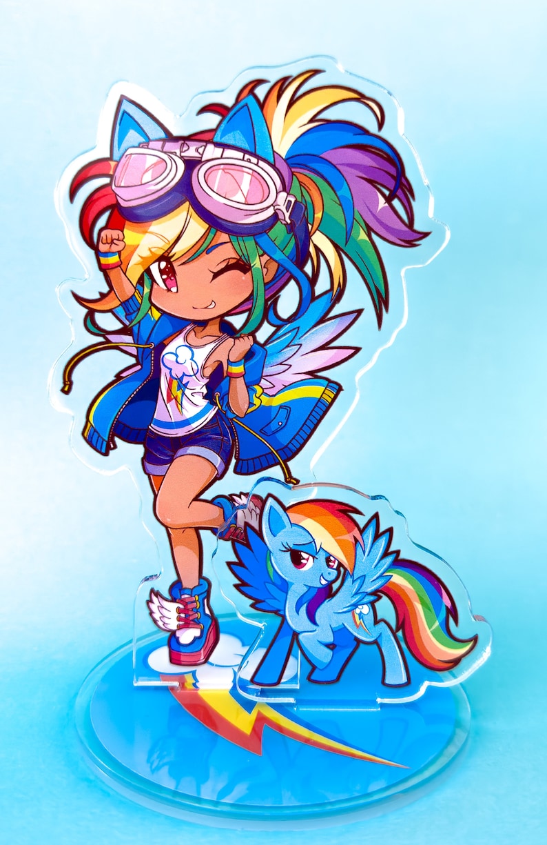 May include: A colorful acrylic stand featuring a cartoon character with rainbow hair, blue wings, and a blue jacket. The character is wearing goggles and has a rainbow tail. The stand also features a smaller cartoon pony with a rainbow tail.