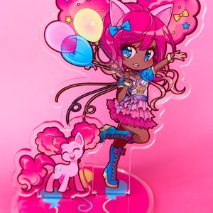 Puede incluir: Un soporte de acr&iacute;lico rosa y azul con un personaje de dibujos animados sosteniendo globos. El personaje tiene el pelo rosa, la piel morena y lleva un atuendo rosa y azul. Un pony rosa con una crin y una cola rosas est&aacute; de pie junto al personaje. El soporte tiene una base rosa con un dise&ntilde;o de espiral.