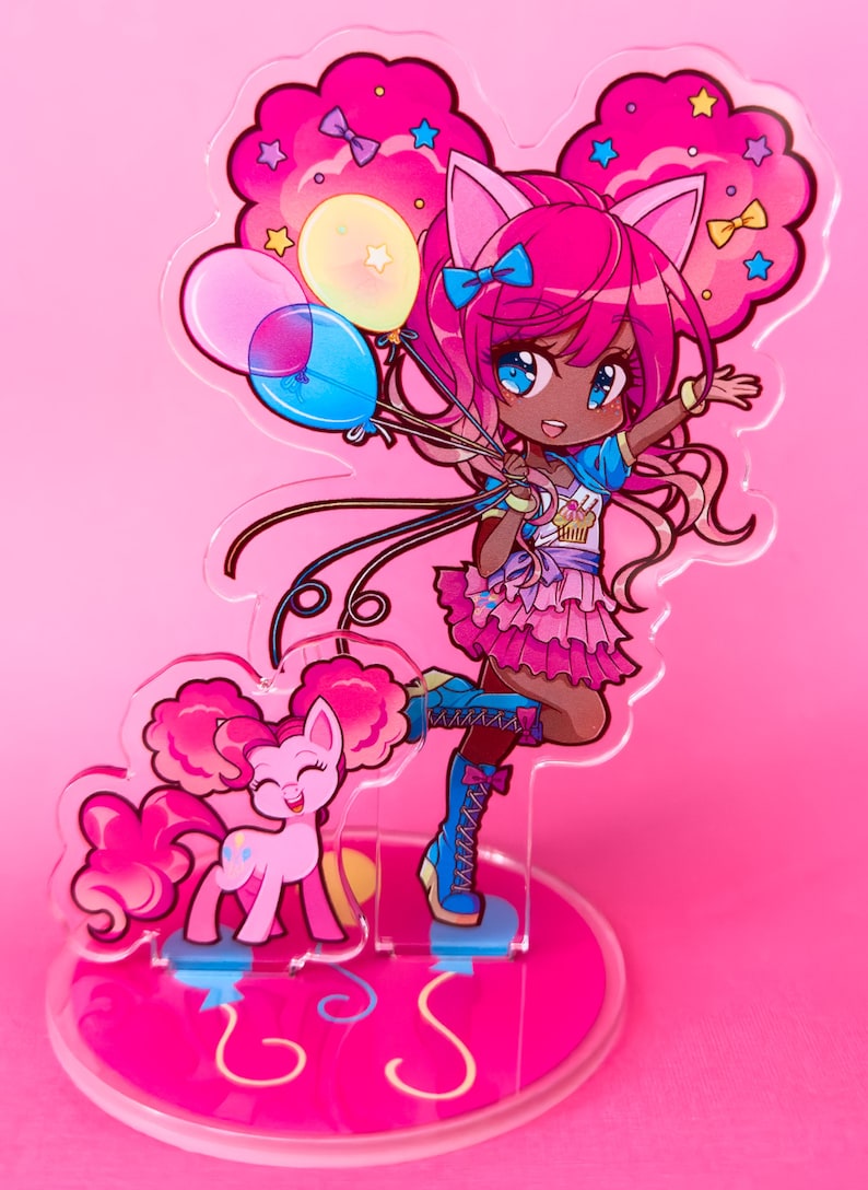 Puede incluir: Un soporte de acr&iacute;lico rosa y azul con un personaje de dibujos animados sosteniendo globos. El personaje tiene el pelo rosa, la piel morena y lleva un atuendo rosa y azul. Un pony rosa con una crin y una cola rosas est&aacute; de pie junto al personaje. El soporte tiene una base rosa con un dise&ntilde;o de espiral.