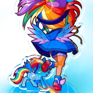 May include: A colorful acrylic stand featuring a cartoon character with rainbow hair, blue wings, and a blue jacket. The character is standing on a rainbow with a smaller cartoon pony beside them. The stand has a blue background with white clouds and the text "KAYOZIA/7237".