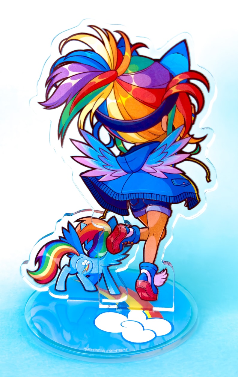 May include: A colorful acrylic stand featuring a cartoon character with rainbow hair, blue wings, and a blue jacket. The character is standing on a rainbow with a smaller cartoon pony beside them. The stand has a blue background with white clouds and the text "KAYOZIA/7237".