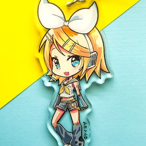 May include: A clear acrylic keychain featuring a cartoon illustration of a female anime character with blonde hair, a white bow, and a blue and black outfit. The character is holding a microphone and has a blue and white headset on. The text "©ケイヨウ" is printed on the bottom right corner of the keychain.