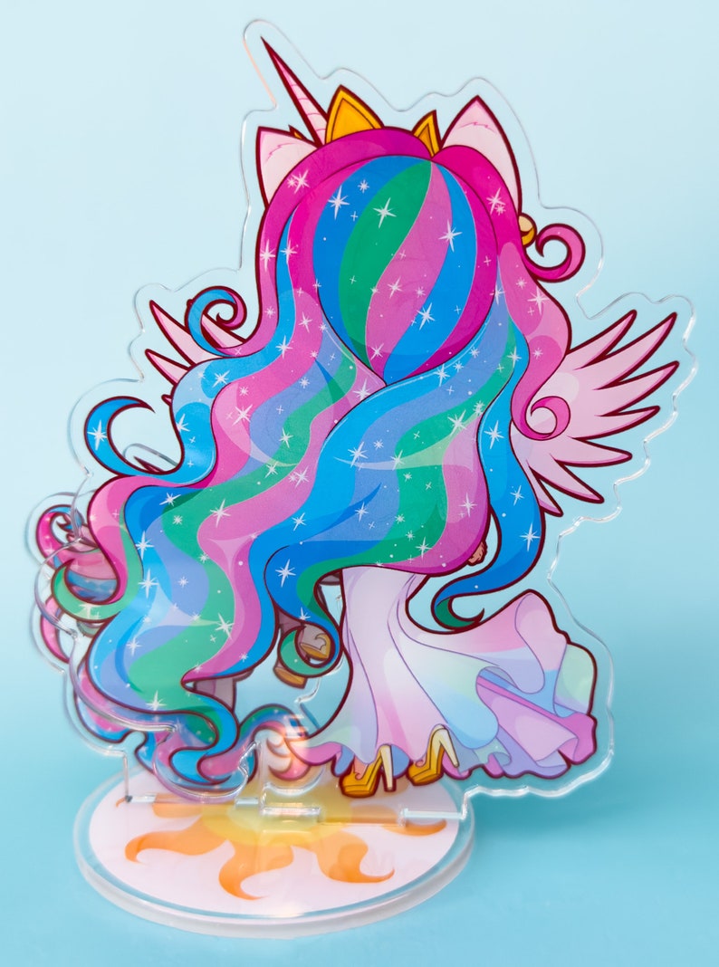 Puede incluir: Un soporte de acr&iacute;lico colorido con una representaci&oacute;n de dibujos animados de la Princesa Celestia de My Little Pony. El soporte es transl&uacute;cido y muestra al personaje con un vestido rosa, azul y verde con una corona dorada y alas. La base del soporte es un sol amarillo.