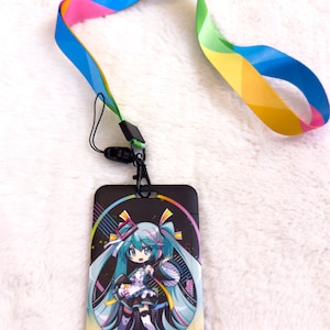 以下が含まれることがあります： レインボーカラーのカラフルなパターンが付いた黒いランヤード。ランヤードには、青い髪と白いドレスを着た漫画のキャラクターのカラフルなイラストが描かれた黒いプラスチック製のバッジホルダーが付いています。バッジホルダーには「初音ミク」の文字が印刷されています。