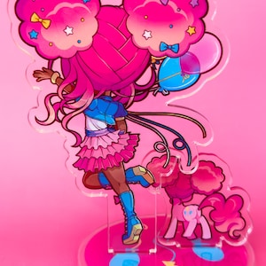 Puede incluir: Un personaje rosa y azul con grandes lazos rosas en el pelo y una falda rosa que sostiene globos. El personaje est&aacute; de pie sobre una base redonda con un dise&ntilde;o rosa y azul. La base tiene el texto "ましろ屋" en japon&eacute;s.