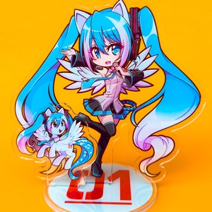 Puede incluir: Un personaje de anime azul y rosa con cabello azul largo y orejas de gato, vistiendo un atuendo blanco y azul, sosteniendo un micr&oacute;fono. El personaje est&aacute; de pie sobre una base de acr&iacute;lico transparente con el n&uacute;mero "01" impreso en ella. Un personaje de anime m&aacute;s peque&ntilde;o, azul y rosa, con alas, est&aacute; de pie junto al personaje m&aacute;s grande.