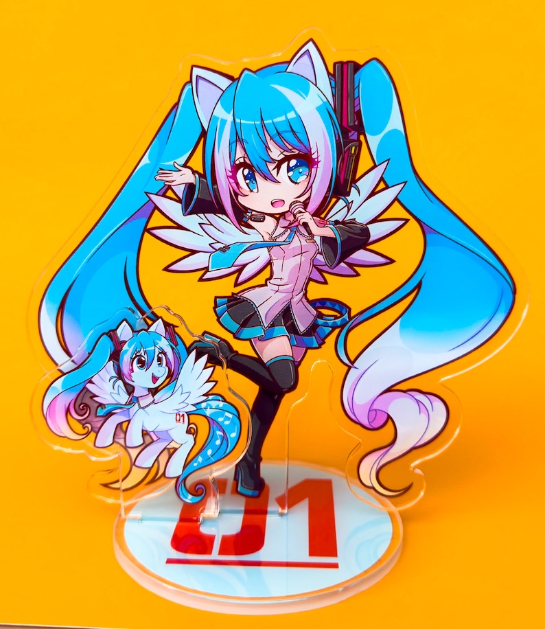 Puede incluir: Un personaje de anime azul y rosa con cabello azul largo y orejas de gato, vistiendo un atuendo blanco y azul, sosteniendo un micr&oacute;fono. El personaje est&aacute; de pie sobre una base de acr&iacute;lico transparente con el n&uacute;mero "01" impreso en ella. Un personaje de anime m&aacute;s peque&ntilde;o, azul y rosa, con alas, est&aacute; de pie junto al personaje m&aacute;s grande.