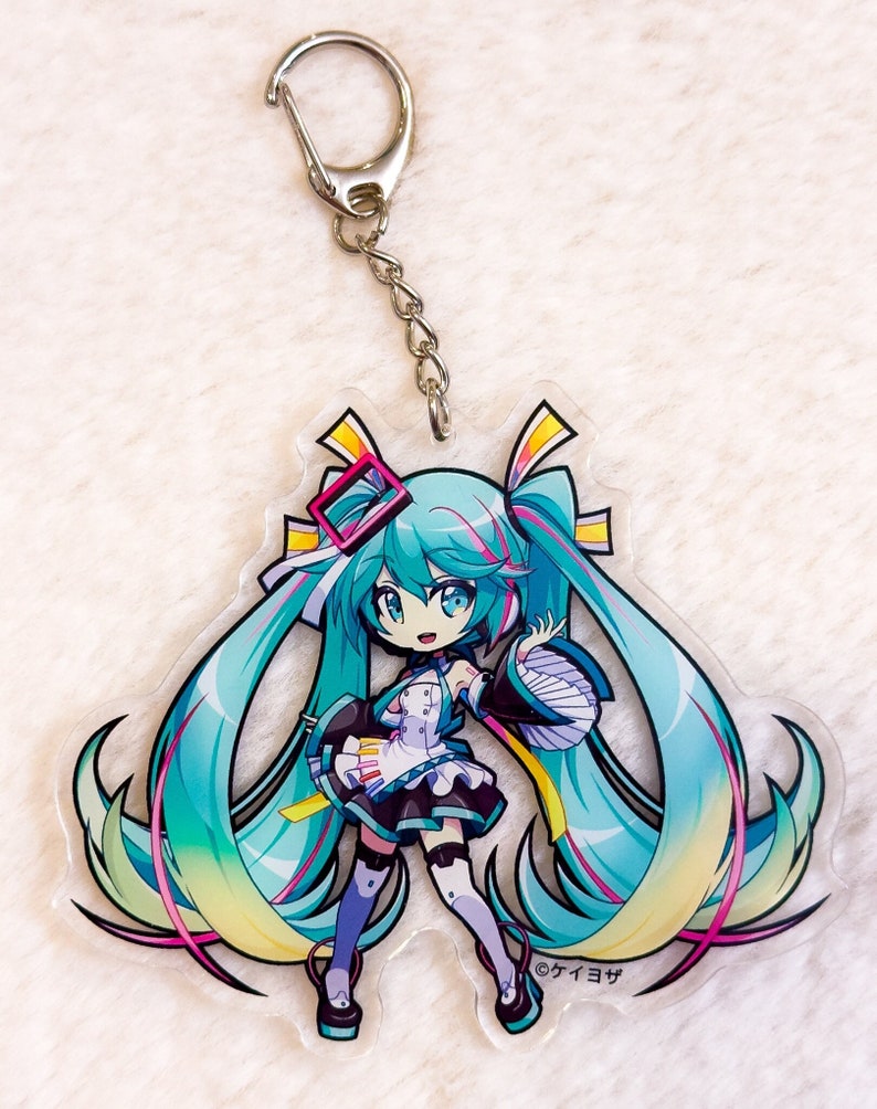 Peut inclure: Un porte-cl&eacute;s en acrylique transparent repr&eacute;sentant une illustration de personnage d'anime aux cheveux bleus avec un n&oelig;ud rose et une robe blanche. Le personnage tient un microphone et a un fond jaune et vert. Le texte "&copy;タイヨウサ" est imprim&eacute; dans le coin inf&eacute;rieur droit du porte-cl&eacute;s.