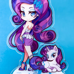 May include: A clear acrylic stand with a purple and white cartoon unicorn character. The unicorn has a blue eye and a pink horn. The stand has two blue diamond shapes on the base.