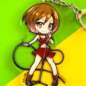 May include: An acrylic keychain featuring a chibi-style character with short brown hair, wearing a red top and skirt, holding a microphone on a stand with a black cord. The character has brown eyes and wears brown boots. The text "ケイヨザ" is printed.