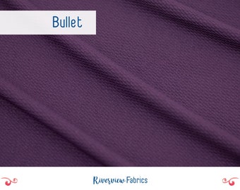 May include: Close-up of a textured, dark purple fabric. The fabric has a subtle, raised pattern. The word "Bullet" is written in white text on a white bar at the top of the image.