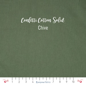 Pode incluir: Uma amostra de tecido em close-up em uma cor verde lisa e discreta. O texto "Confetti Cotton Solid" e "Chive" está escrito em branco em itálico. Uma régua está na parte inferior da imagem, com o logotipo da Riverview Fabrics.