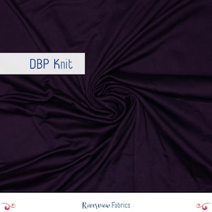 Pode incluir: Tecido de malha DBP roxo escuro com uma textura macia e fluida. O tecido é reunido em um padrão de redemoinho, com o texto "DBP Knit" em uma etiqueta retangular branca. O logotipo da Riverview Fabrics está na parte inferior.