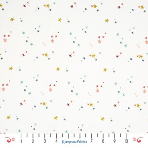 Peut inclure: Un tissu blanc avec un motif dispersé de petites étoiles multicolores dans des tons jaune, bleu sarcelle, bleu foncé et corail. Une règle en bas indique une échelle de 10 centimètres, avec le texte Riverview Fabrics imprimé au centre.