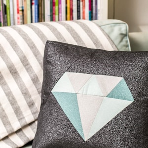 May include: A black pillow with a large diamond-shaped design in shades of blue and white. The diamond is made of fabric pieces sewn together.